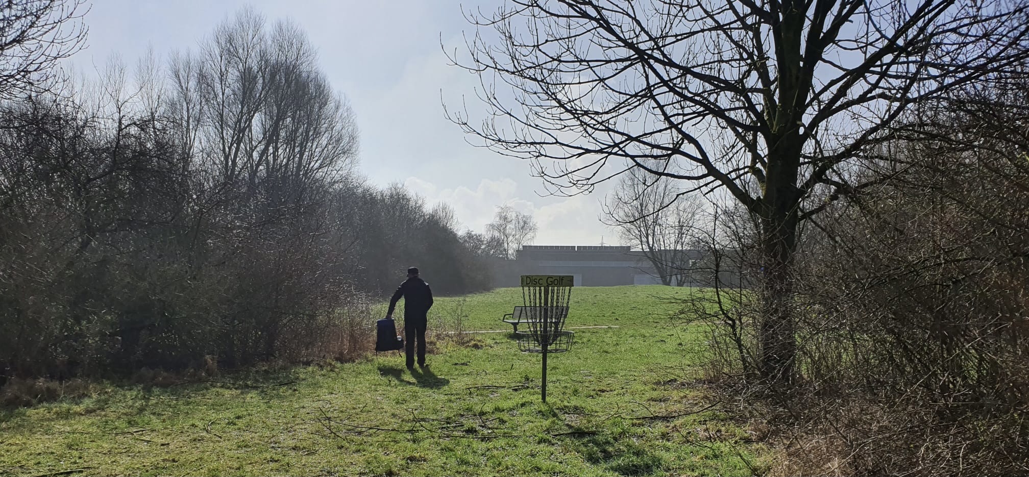 mann trägt Rucksack mit discgolfscheiben zum discgolfkorb